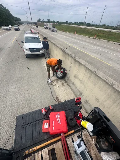 Technician servicing a removed tire on a highway shoulder beside a service truck loaded with tools