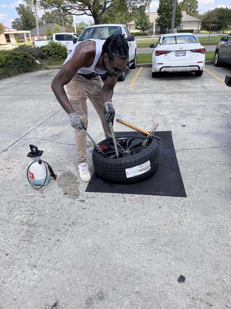 Technician mounting a tire onto a wheel with pry bars while kneeling on a ground mat
