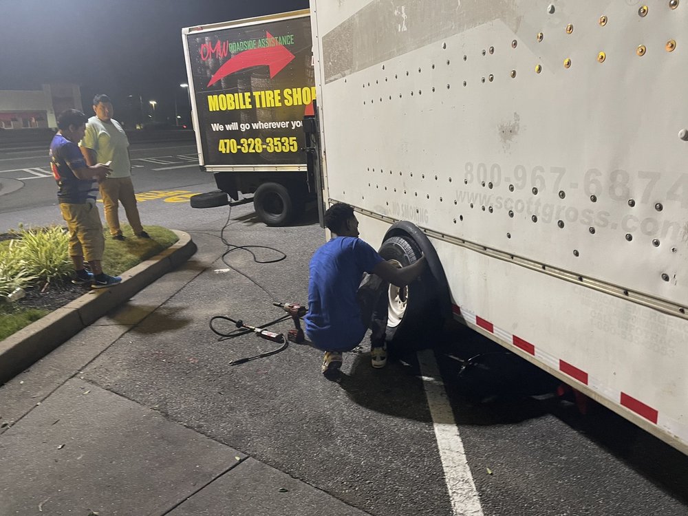 Technician crouched at night mounting a wheel onto a large box truck