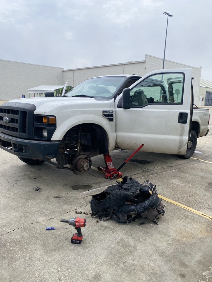 Pickup truck raised on a jack with the wheel removed and the shredded remains of a blown tire on the ground