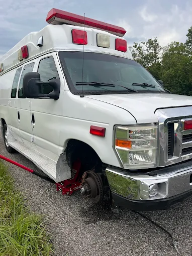 Van raised on a red hydraulic jack with the front wheel removed on a road shoulder
