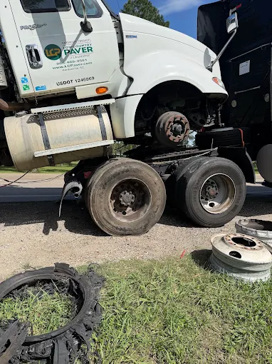 Blown commercial truck tire with shredded tread and two removed rims lying on the ground