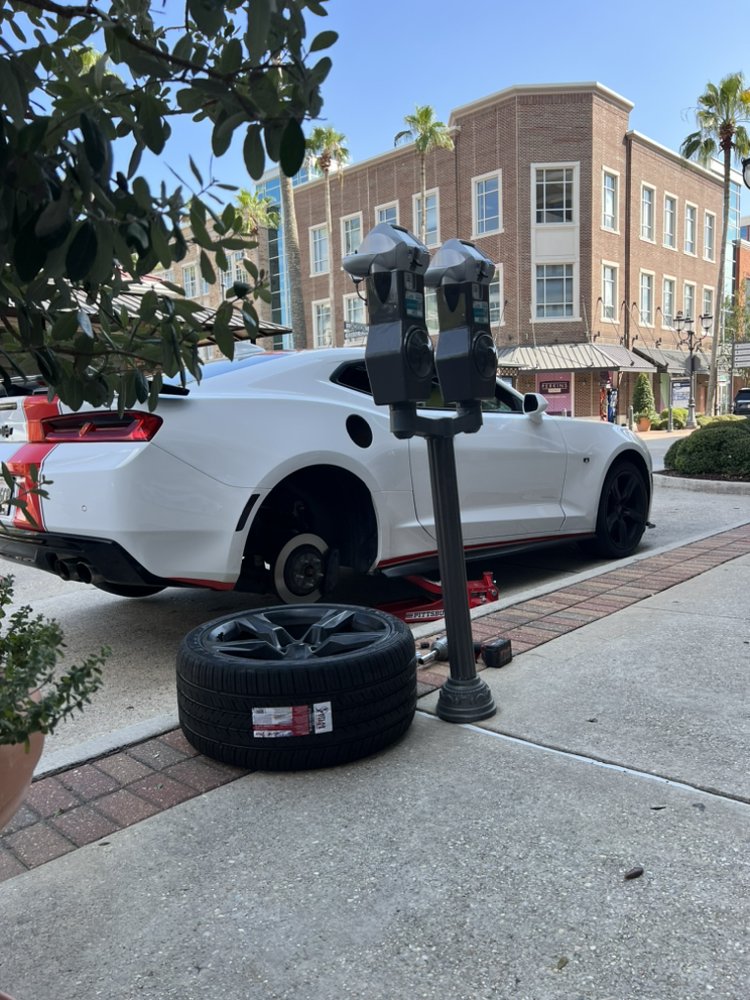 Sports car raised on a jack at a city curb with a new tire waiting on the sidewalk